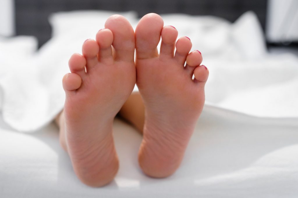 Girl feet in a white bed in the morning. Enjoy and relax in the morning. Smooth skin on the heels