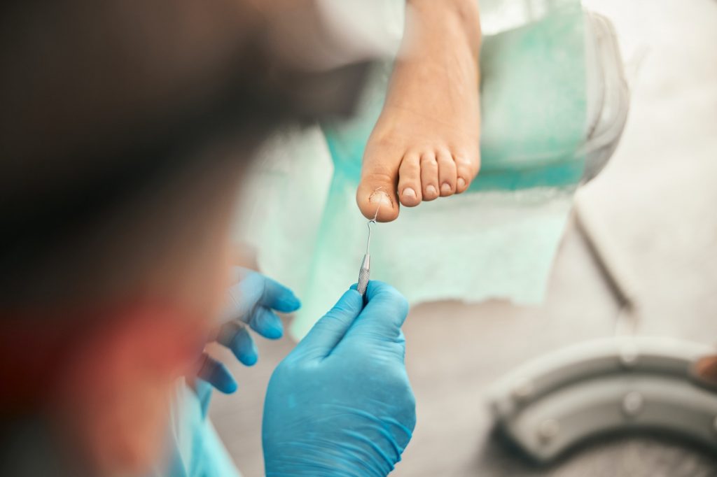 Attentive podologist doing medical pedicure for visitor