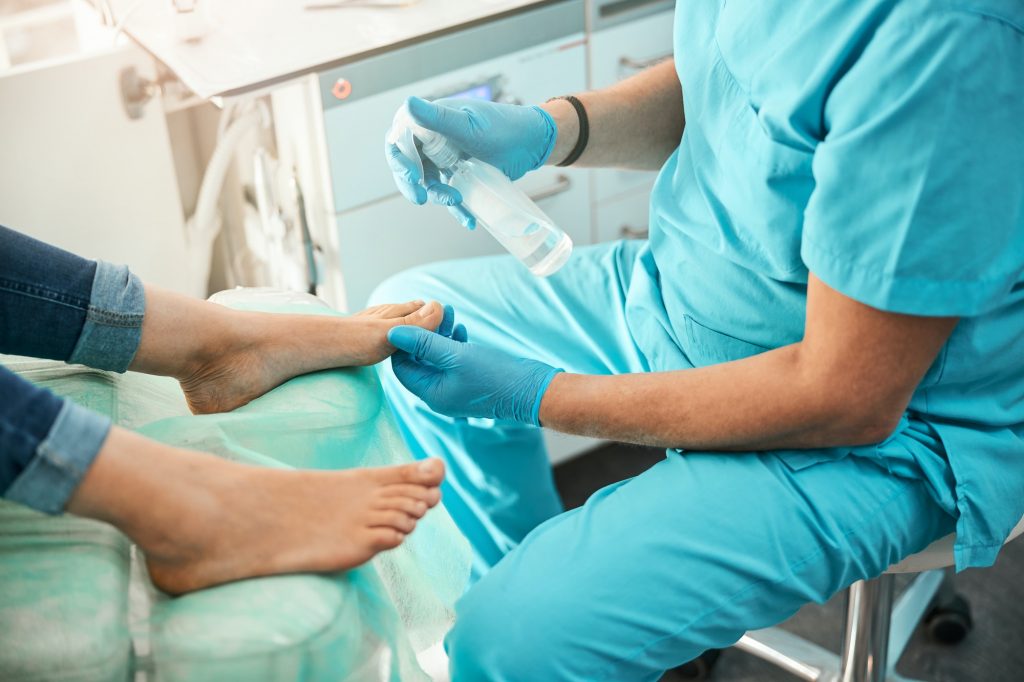 Competent podologist spraying antibacterial disinfectant on nails